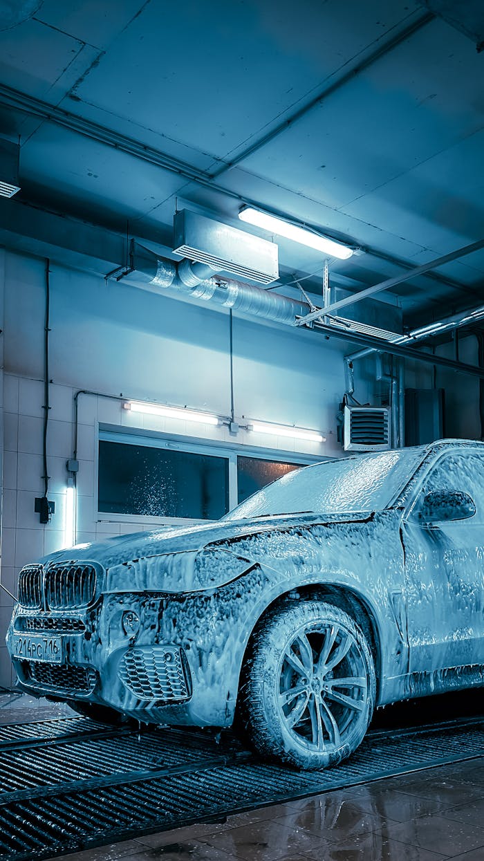 Luxury SUV covered in foam inside a modern car wash station enhanced by blue lighting.